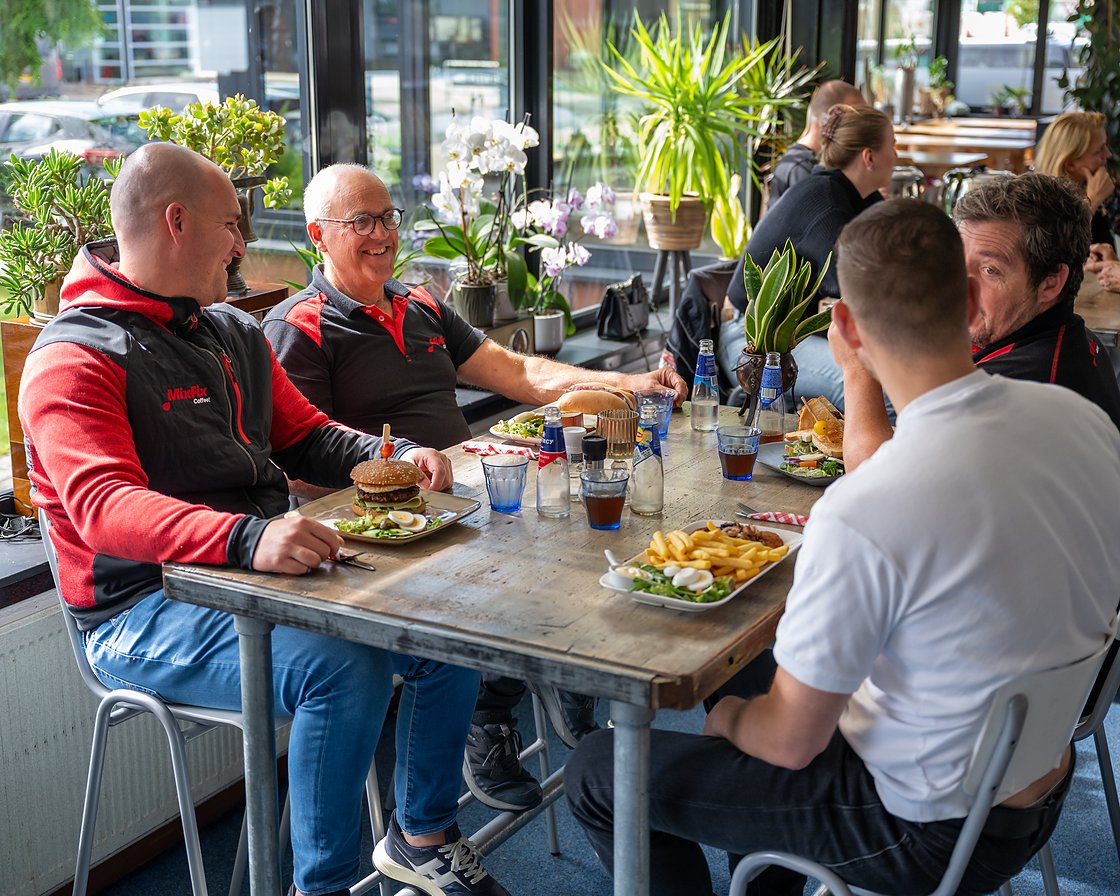 een gezelschap aan de lange tafel met de lunch erop